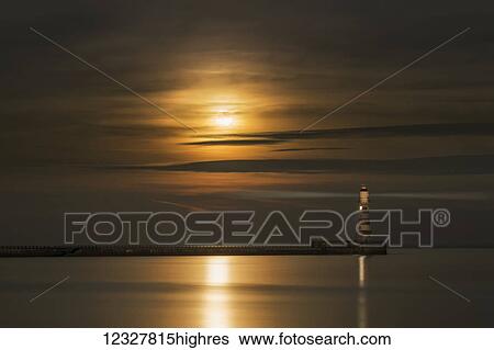 Roker lighthouse casts a light with the golden sunlight shining through cloud and reflecting on tranquil water; Sunderland, Tyne and Wear, England View Large Photo Image Stock Photograph - Roker lighthouse casts a light with the golden sunlight shining through cloud and reflecting on tranquil water; Sunderland, Tyne and Wear, England. Fotosearch