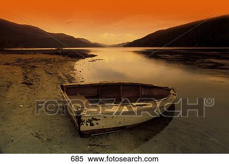 Rowboat at water's edge against sunset backdrop View Large Photo Image Stock Photography - Rowboat at water's edge against sunset backdrop. Fotosearch