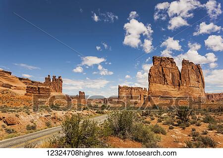Stock Photograph - Rugged rock formations and shrubs in the desert, with a road passing through; Arizona, United States of America. Fotosearch