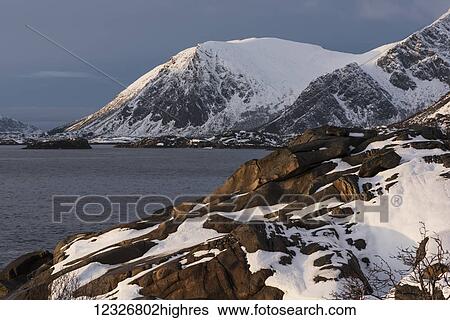 Stock Photograph - Rugged, snow covered mountains along the coastline of an island; Lofoten Islands, Nordland, Norway. Fotosearch