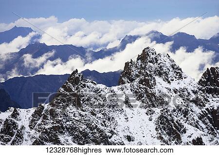 Stock Photograph - Rugged snow covered peaks of the Kenai Mountains with blue sky and cloud; Alaska, United States of America. Fotosearch