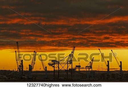 Stock Photograph - Silhouette of cranes on a construction site against a dramatic red and yellow sky at sunset; South Shields, Tyne and Wear, England. Fotosearch