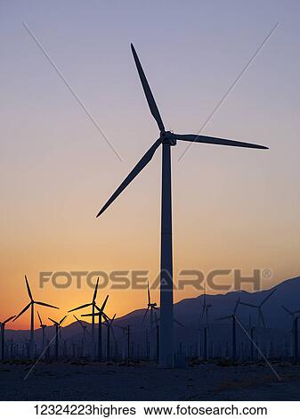 Stock Photograph - Silhouette of wind turbines in a field with a mountain range in the distance at sunset; Palm Springs, California, United States of America. Fotosearch