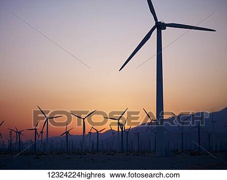 Stock Photograph - Silhouette of wind turbines in a field with a mountain range in the distance at sunset; Palm Springs, California, United States of America. Fotosearch