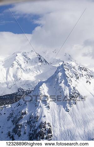 Stock Photograph - Snow covered Kenai Mountains with blue sky peaking out from the clouds, Kachemak Bay State Park; Alaska, United States of America. Fotosearch