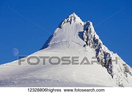 Snow covered mountain peak against a blue sky with a faint moon in the distance; Alaska, United States of America View Large Photo Image Stock Photograph - Snow covered mountain peak against a blue sky with a faint moon in the distance; Alaska, United States of America. Fotosearch