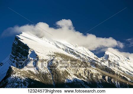 Snow covered mountain peak with frosted evergreen trees, blue sky and clouds along peak; Banff, Alberta, Canada View Large Photo Image Stock Photograph - Snow covered mountain peak with frosted evergreen trees, blue sky and clouds along peak; Banff, Alberta, Canada. Fotosearch