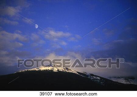Stock Photo - Snow covered mountain with clouds and moon backdrop. Fotosearch
