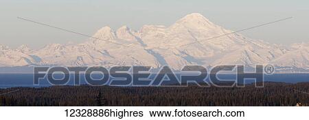 Stock Photograph - Snow covered mountains range in the distance with ocean and forest in the foreground; Alaska, United States of America. Fotosearch