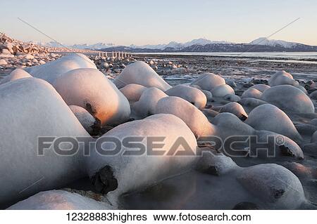 Snow covered rocks and beach with a view of the ocean and mountains along the coastline; Alaska, United States of America View Large Photo Image Stock Photograph - Snow covered rocks and beach with a view of the ocean and mountains along the coastline; Alaska, United States of America. Fotosearch