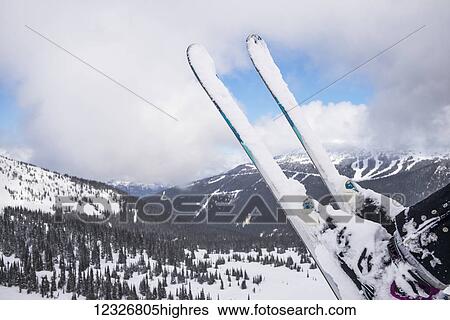 Stock Photograph - Snow covered skis on a skier sitting on a chairlift with a view of the snow covered forest and mountains at a ski resort; Whistler, British Columbia, Canada. Fotosearch
