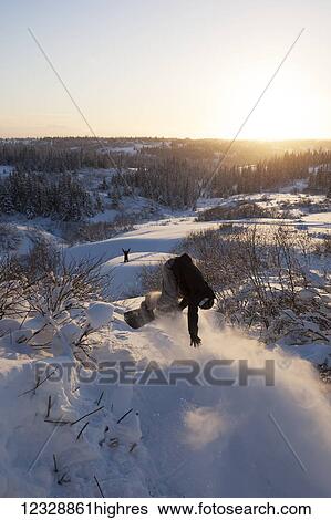 Stock Photograph - Snowboarder in mid-air with a friend cheering with arms raised on a hill below; Alaska, United States of America. Fotosearch