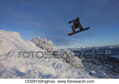 Stock Photograph - Snowboarder in mid-jump with the Kachemak Bay in the background, Homer, Southcentral Alaska, USA. Fotosearch
