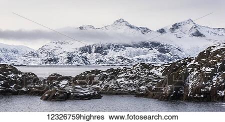 Stock Photograph - Snowy landscape of rugged mountains and ocean water; Nordland, Norway. Fotosearch