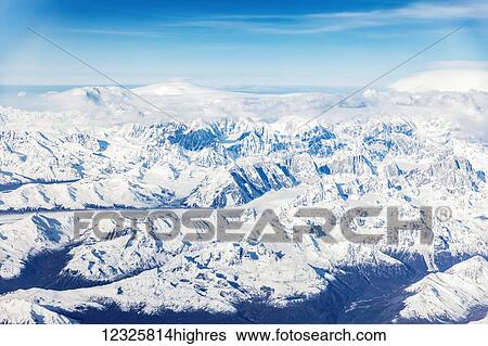 Stock Photograph - Snowy mountain peaks rising above low altitude clouds in the Denali Mountain range, the sun casting shadows in the low valleys below, South-central Alaska; Alaska, United States of America. Fotosearch