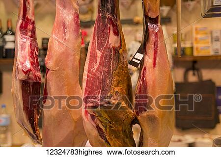 Stock Photograph - Spanish ham hung in a shop in Boqueria Market, one of the most famous markets around Spain and the most famous in Barcelona; Barcelona, Catalonia, Spain. Fotosearch