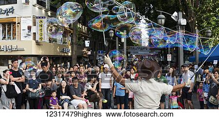 Spectators watch a street performer make bubble art with long wands; Seoul, South Korea View Large Photo Image Stock Photograph - Spectators watch a street performer make bubble art with long wands; Seoul, South Korea. Fotosearch