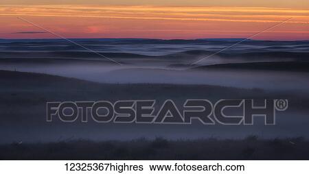 Stock Photograph - Sunrise colour and fog coat the Grasslands National Park in an eerie mist; Saskatchewan, Canada. Fotosearch