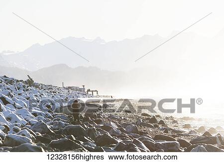 Stock Photograph - Surfer on a rocky shore along Kachemak Bay, Homer Spit, Kenai Peninsula, Southcentral Alaska, USA. Fotosearch