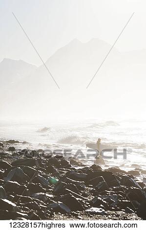 Stock Photograph - Surfer on a rocky shore along Kachemak Bay, Homer Spit, Kenai Peninsula, Southcentral Alaska, USA. Fotosearch