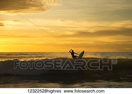 Surfer riding a wave at sunset, Dreamland beach; Bali Island, Indonesia View Large Photo Image Stock Photograph - Surfer riding a wave at sunset, Dreamland beach; Bali Island, Indonesia. Fotosearch