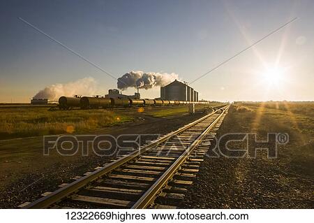 Stock Photograph - The Poet Biorefinery, an ethanol producer, and corn field, with train tracks in the foreground, near Groton; South Dakota, United States of America. Fotosearch