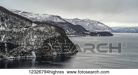 Stock Photograph - The rugged coastline and tranquil ocean water under a cloudy sky; Nordland, Norway. Fotosearch