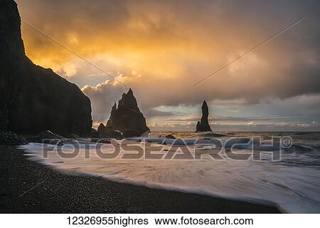 Stock Photograph - The sea stacks known as Reynisdrangar with waves at sunrise, South Coast; Iceland. Fotosearch
