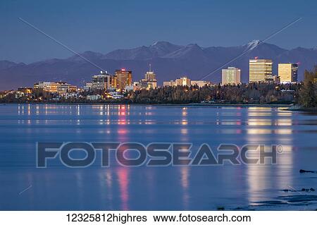 Stock Photograph - The setting sun reflects off of office buildings in downtown Anchorage, seen from Earthquake Park, the Chugach Mountains in the background, South-central Alaska; Anchorage, Alaska, United States of America. Fotosearch