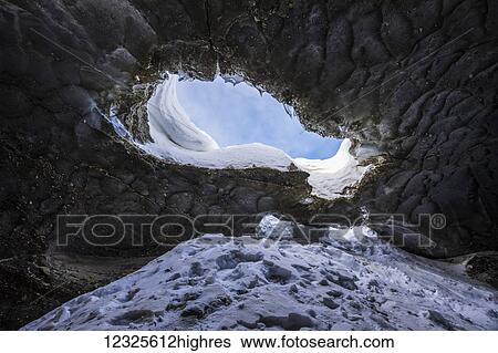 Stock Photograph - The sky is visible through a hole in the ceiling of this Castner Glacier ice cave in the Alaska Range; Alaska, United States of America. Fotosearch