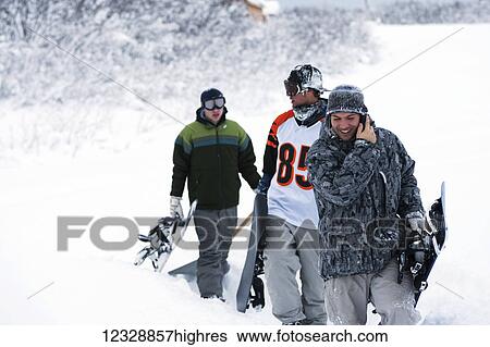 Three snowboarders walking up a trail in deep snow with their snowboards, one snowboarder talking on a cell phone; Alaska, United States of America View Large Photo Image Stock Photograph - Three snowboarders walking up a trail in deep snow with their snowboards, one snowboarder talking on a cell phone; Alaska, United States of America. Fotosearch