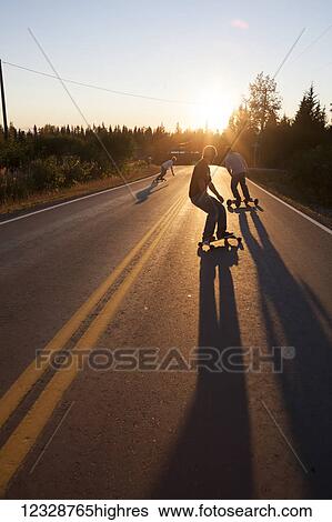 Three young men skateboarding down a road at sunset; Homer, Alaska, United States of America View Large Photo Image Stock Photograph - Three young men skateboarding down a road at sunset; Homer, Alaska, United States of America. Fotosearch