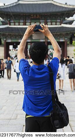 Stock Photograph - Tourist holds a camera up for a photograph at Gyeongbokgung Palace; Seoul, Korea. Fotosearch