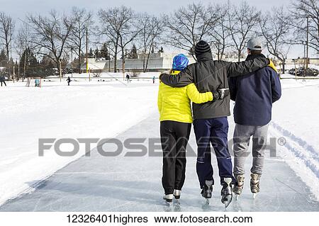 Two males and one female skating arm in arm on freshly groomed ice on pond with community centre in the background; Calgary, Alberta, Canada View Large Photo Image Stock Photograph - Two males and one female skating arm in arm on freshly groomed ice on pond with community centre in the background; Calgary, Alberta, Canada. Fotosearch