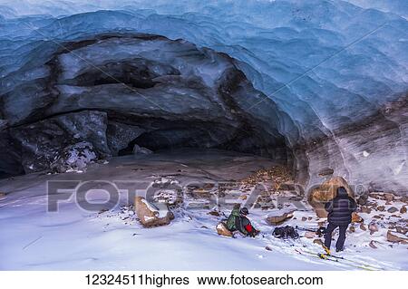 Stock Photograph - Two men pack up their gear after exploring an Augustana Glacier ice cave in the winter; Alaska, United States of America. Fotosearch