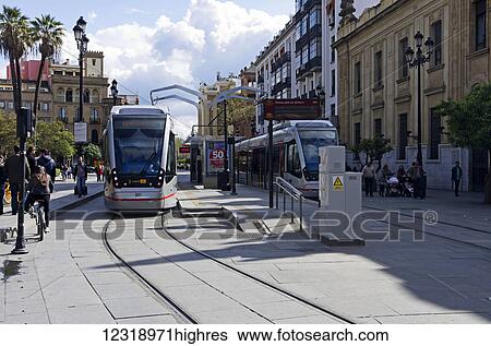 Stock Photograph - Two modern trams stopped at Santa Cruz center of Seville; Seville, Andalusia, Spain. Fotosearch