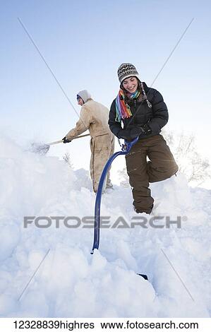 Stock Photograph - Two people shoveling deep snow; Alaska, United States of America. Fotosearch
