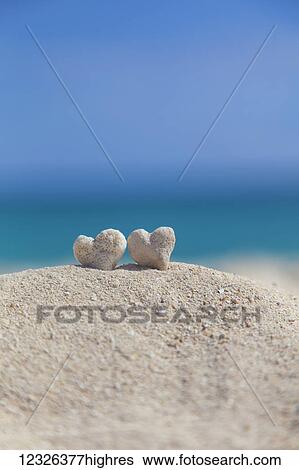 Stock Photograph - Two white heart shaped coral rocks placed together on sand at the beach; Honolulu, Oahu, Hawaii, United States of America. Fotosearch