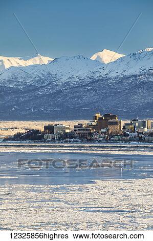 Stock Photograph - View of downtown Anchorage in winter and the snow-capped Chugach Mountains beyond seen from Point MacKenzie, the skies in the background clear and bright, sea ice covering Cook Inlet in the foreground, South-central Alaska; Anchorage, Alaska, United.... Fotosearch