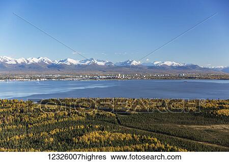 Stock Photograph - View of downtown Anchorage, Point MacKenzie in the foreground, the snow covered Chugach Mountains in the distance, South-central Alaska; Anchorage, Alaska, United States of America. Fotosearch