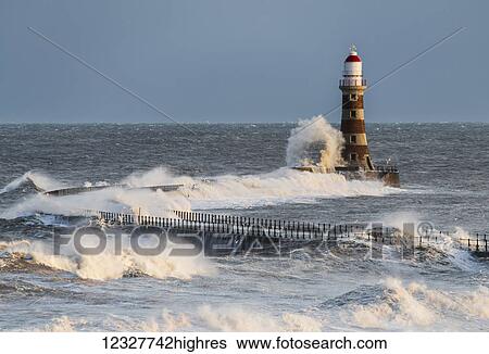Stock Photograph - Waves splashing against Roker lighthouse at the end of a pier; Sunderland, Tyne and Wear, England. Fotosearch