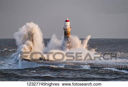 Stock Photograph - Waves splashing against Roker lighthouse at the end of a pier; Sunderland, Tyne and Wear, England. Fotosearch