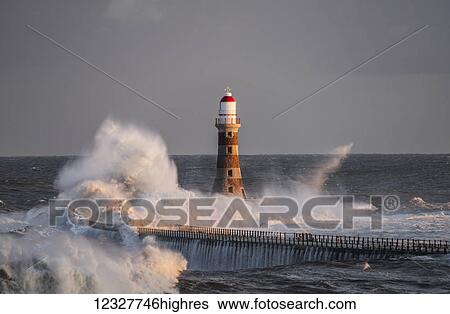 Stock Photograph - Waves splashing against Roker lighthouse at the end of a pier; Sunderland, Tyne and Wear, England. Fotosearch