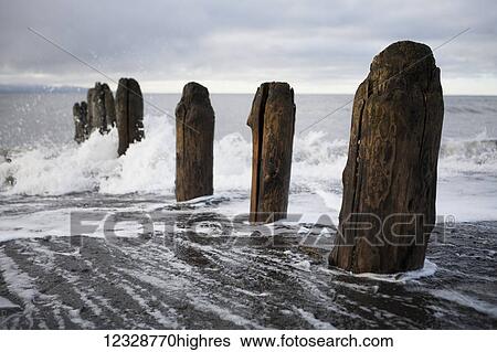 Stock Photograph - Waves splashing against wooden tide posts in Kachemak Bay; Alaska, United States of America. Fotosearch