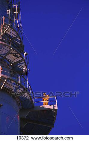 Stock Image - Worker on processing tower of an oil refinery. Fotosearch