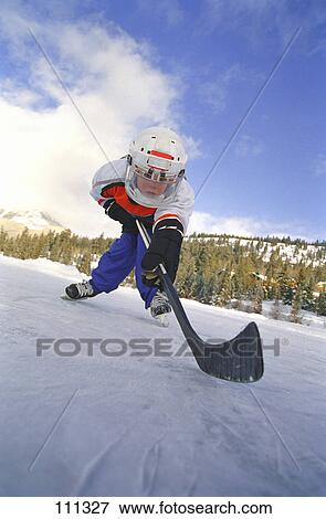 Stock Photo - Young boy playing ice hockey outdoors. Fotosearch