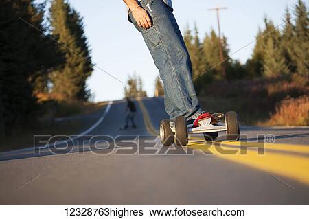 Stock Photograph - Young men skateboarding down a road; Homer, Alaska, United States of America. Fotosearch