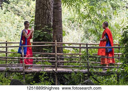 Stock Photograph - A buddhist monk takes a photograph of another monk by the Tad Hang Waterfall, Tad Lo, Bolaven Plateau; Champasak, Laos. Fotosearch