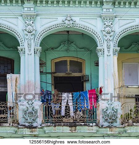 Stock Photograph - A building with ornate and decorative facade and a clothesline hanging across a balcony where a man sits looking out; Havana, Cuba. Fotosearch
