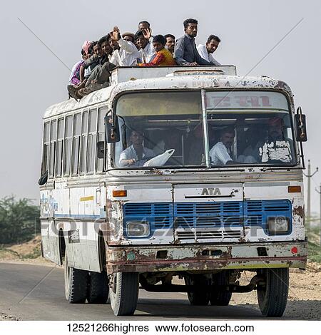 Stock Photograph - A bus full of people and passengers riding on the roof; Jaisalmer, Rajasthan, India. Fotosearch